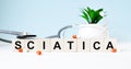 The word SCIATICA is written on wooden cubes near a stethoscope on a wooden background. Medical concept