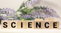 The word SCIENCE is written on wooden cubes on a wooden background next to a pen and glasses