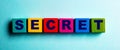 The word SECRET is written on colorful wooden cubes on a light blue background