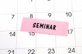 The word Seminar written on a pink sticky note posted on a calendar or planner page. Closeup of a personal agenda