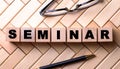 The word SEMINAR is written on wooden cubes on a wooden background next to a pen and glasses