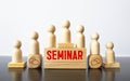 The word SEMINAR is written on wooden cubes on a wooden background next to a pen and glasses