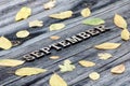 Word September, wooden letters. Frame of yellow leaves, wooden background
