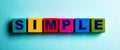 The word SIMPLE is written on multicolored bright wooden cubes on a light blue background