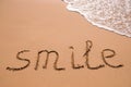 Word Smile hand written in the sand with a sea wave. Close up sand texture on beach in summer Royalty Free Stock Photo