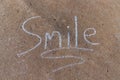 The word Smile written with sidewalk chalk on gray concrete