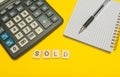 Word sold made with wood letters on yellow background and modern calculator with pen and notebook. Copy space. Economy, money Royalty Free Stock Photo