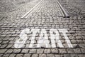 Word START is written on cobbled paved road with rails - beginning of road, new life.