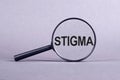 The word STIGMA is written on a magnifying glass on a light violrt background