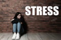 Word STRESS and depressed young girl sitting on floor near wall