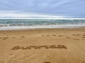 Word Summer handwritten on sandy beach with soft ocean wave on background