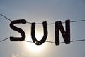 Word SUN with metallic letters hanging against the sky with a flowing sun