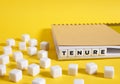 The word tenure written on cubes in a notebook on yellow background