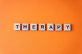 Word therapy. The phrase is laid out in wooden letters top view. Orange flat lay background. Destressing hobby concept. Royalty Free Stock Photo