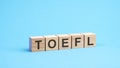 word TOEFL made with wood building blocks. text is written in black letters, blue background