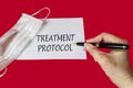 The word treatment protocol is written by a doctor on a red background near a medical protective mask. Medical concept