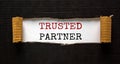 The word `trusted partner` appearing behind torn black paper. Beautiful background. Business concept