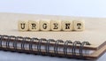 Word URGENT made with letters on wooden blocks on wooden notepad