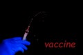 The word Vaccine in the corner, isolate, copy space. A hand in a disposable glove holds a syringe with a red vaccine