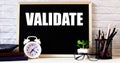 The word VALIDATE is written on the chalkboard next to the white alarm clock, glasses, potted plant, and pencils in a stand