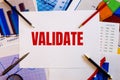 The word VALIDATE is written on a white background near colored graphs, pens and pencils. Business concept