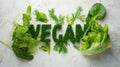 Word Vegan, title text lined up into word made from green lettuce on white table with parsley, spinach broccoli, dill