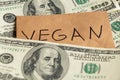 The word vegan is written on paper on the background of a one hundred dollar bill, the refusal of meat, the price of