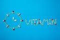 Word vitamin written with colorful pills on a blue background with clock.