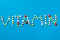 Word vitamin written with colorful pills on a blue background, the concept of supplement needed for a healthy life.