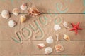 Word voyage written on sand among seashells