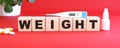 The word WEIGHT is made of wooden cubes on a red background. Medical concept