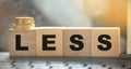 Less word on wooden cubic blocks with letters and stack of coins on it. Selective focus. Spend less or cut costs business concept Royalty Free Stock Photo