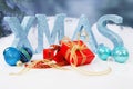 The word Xmas in blue glitter letters with balls and presents