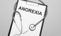 The words anorexia is written on white paper on a grey background near a stethoscope. Medical concept