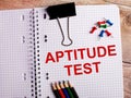 The words APTITUDE TEST is written in a notebook near multi-colored pencils and buttons on a wooden background Royalty Free Stock Photo