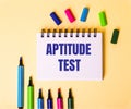 The words APTITUDE TEST written in a white notebook on a beige background near multi-colored markers Royalty Free Stock Photo