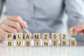 Words business plan 2023 collected from wooden cubes and businessperson with pen in background.