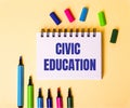 The words CIVIC EDUCATION written in a white notebook on a beige background near multi-colored markers