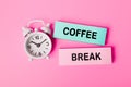 The words Coffee Break written on paper note near white alarm clock on pink background. Closeup of a personal agenda