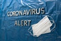 Words coronavirus alert laid with silver letters on crumpled blue plastic coat - in perspective view with face masks
