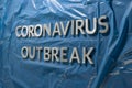 The words coronavirus outbreak laid with silver metal letters on crumpled blue plastic film Royalty Free Stock Photo