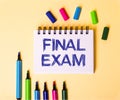The words FINAL EXAM written in a white notebook on a beige background near multi-colored markers Royalty Free Stock Photo