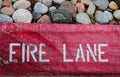 Fire Lane stenciled on a scuffed and chipped red painted curb with rocks from flower bed on top