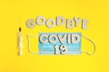 Words GOODBYE COVID 19 from wooden letters, syringe and facemask. Vaccination and the end of epidemic concept.