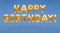 Words HAPPY BIRTHDAY made of golden inflatable balloons floating on blue background. Gold foil helium balloons forming phrase. Royalty Free Stock Photo