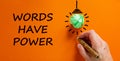 Words have power symbol. Businessman writing text `Words have power`, isolated on beautiful orange background. Light bulb icon.