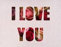 The words I Love You cut out of a white gray piece of paper with roses visible through the holes