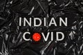 words indian covid laid with silver metal letters on crumpled black plastic bag background with small virus model Royalty Free Stock Photo