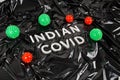 words indian covid laid with silver metal letters on crumpled black plastic bag background with small virus models Royalty Free Stock Photo