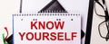 The words KNOW YOURSELF is written in red in a white notebook next to black-framed glasses Royalty Free Stock Photo
